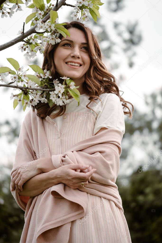 Beautiful happy young woman enjoying flowers and smelling blossom tree in the spring garden