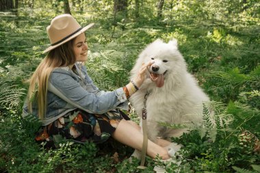 Genç ve güzel bir kadın ormanda bembeyaz tüylü köpeğiyle vakit geçiriyor.