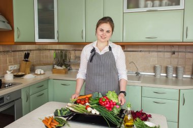 Mutlu Kadın mutfak arka planında taze sebze malzemeleriyle dolu bir tepsi tutuyor. Sağlıklı vejetaryen yemekleri. 