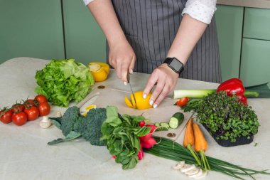 Kadın mutfakta sebze salatası hazırlıyor ve masandaki malzemeleri kesiyor. Sağlıklı vejetaryen yemekleri. 