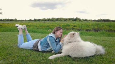 Genç, güzel bir kadın, tüylü ve mutlu köpeğiyle çimenlerde yatıyor.