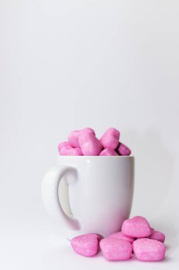 Beyaz arka planda beyaz bir fincanda pembe kalp şekilli şekerler yığını