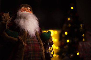 Noel Baba hediye dolu büyük bir çanta taşıyor, Noel ağacının yanında.