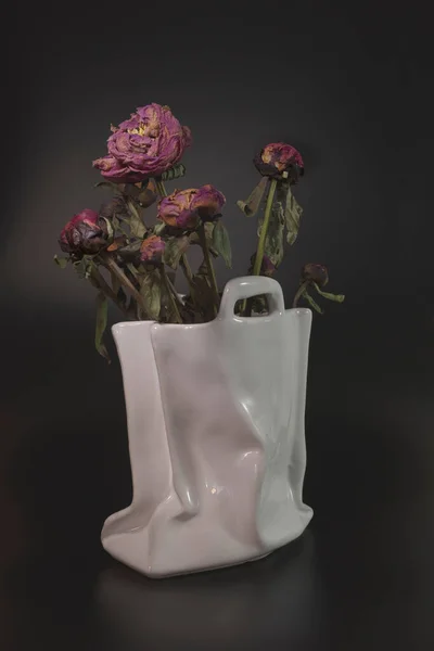 Wilted flowers, peonies in a white ceramic vase in the form of a bag