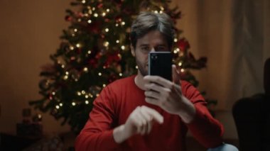 Mutlu adam dekore edilmiş Noel ağacının yanında selfie çekiyor.