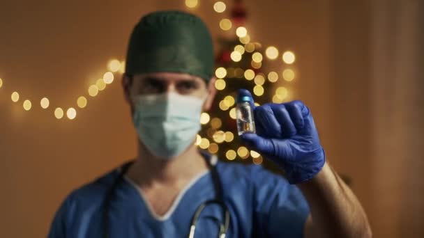 背景にクリスマスライトの付いたコロナウイルスワクチンをマスクした男性医師 — ストック動画