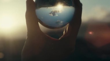 Günbatımında gökyüzü yansıması olan cam küreyi tutan adamın görüntüleri. 