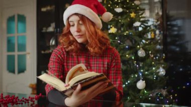 Videonun arkasında noel süsleri olan kitap okuyan genç bir kadın. 