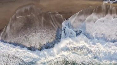 Aerial vertical of stormy waves with foam of ocean and beach