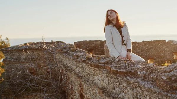 Gadis cantik dengan gaun putih menjelajahi sebuah kastil Italia kuno saat matahari terbenam — Stok Foto