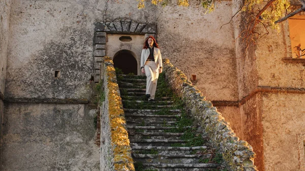 Gadis cantik dengan gaun putih datang menuruni tangga pintu masuk sebuah kastil — Stok Foto
