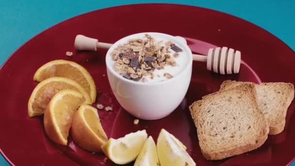 Copa de yogur blanco fresco con granola crujiente en el interior gira en un plato rojo — Vídeo de stock