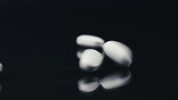 Белые таблетки падают на поверхность черного зеркала — стоковое видео
