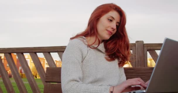 Молода дівчина з ноутбуком стежить за уроком, що сидить на лавці в університеті — стокове відео