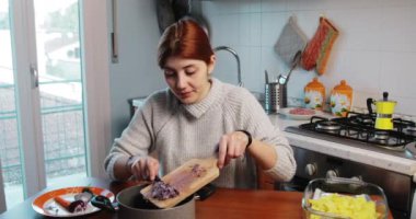 Kız ev yapımı yemek için kızartma tavasına soğan döküyor.