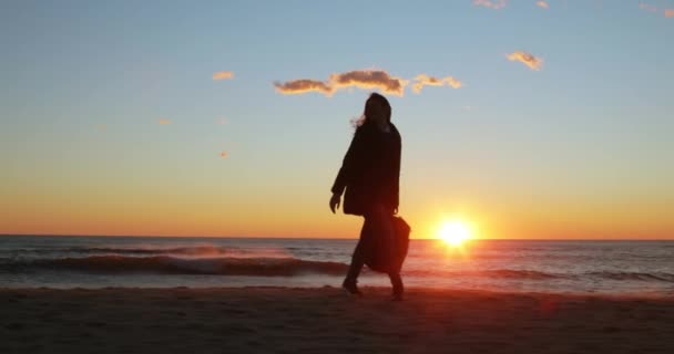 Silhuett av ung flicka med ryggsäck glatt danser vid soluppgången på stranden — Stockvideo