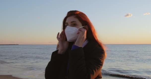 Flicka med rött hår tar av sig masken och andas ren luft nära havet — Stockvideo