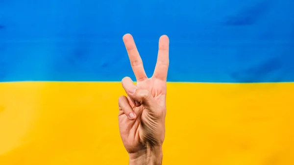 Hand in victory symbol with Ukrainian flag for background — Stock Photo, Image