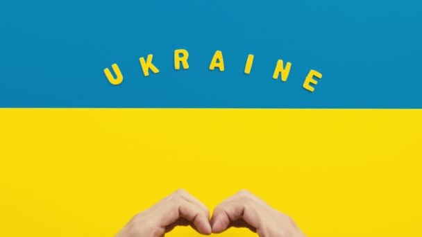 Руки делают символ сердца на флаге Украины в знак солидарности с войной — стоковое видео