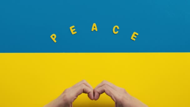 Tangan membuat simbol hati pada bendera Ukraina dengan tulisan damai — Stok Video