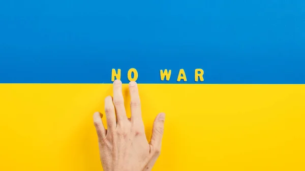 Hånd skriver med bokstaver ingen krig på Ukrainas flagg. – stockfoto