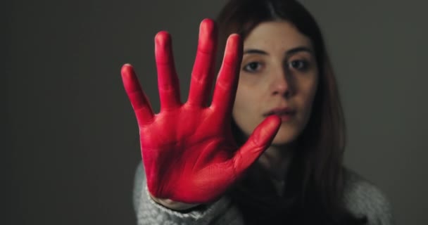 Сумна дівчина піднімає руку пофарбовану в червоний колір, щоб зупинитися і протестувати проти насильства — стокове відео