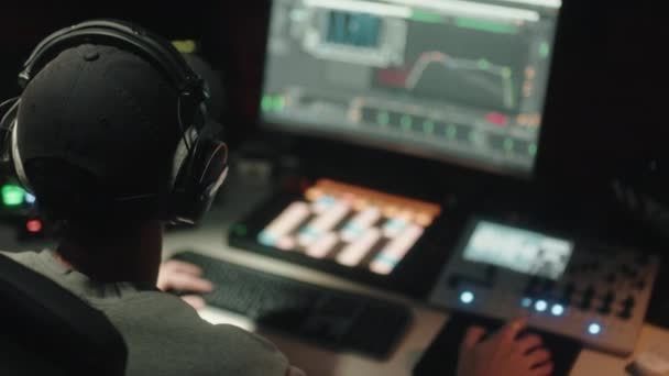 Ingeniero de sonido visto sentado por detrás utiliza la computadora para mezclar música de audio — Vídeos de Stock