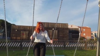 Genç güzel kızıl saçlı kız parkta salıncakla oynamaktan hoşlanıyor.