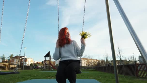 Молода красива дівчина червоного волосся насолоджується в парку граючи з гойдалками — стокове відео