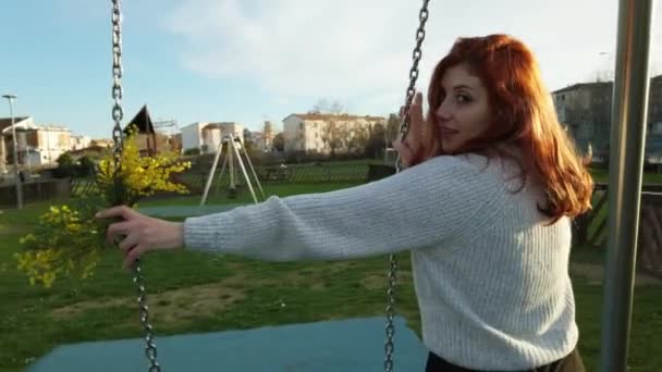 若いです美しい赤い髪の女の子楽しみますザ公園でプレイとともにザスイング — ストック動画