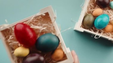 El masaya bir kutu Paskalya yumurtası bırakıyor, açık mavi arka plan.
