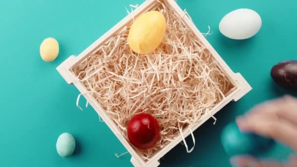 Uma mão de homem está colocando os ovos de Páscoa coloridos na cesta — Vídeo de Stock