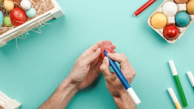 Bir adamın eli renkli Paskalya yumurtaları boyuyor.