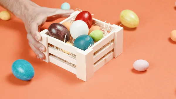 Uma mão de homem está colocando os ovos de Páscoa coloridos na cesta — Fotografia de Stock
