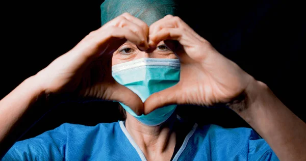 Doutor faz o símbolo do coração com máscara e fundo preto — Fotografia de Stock