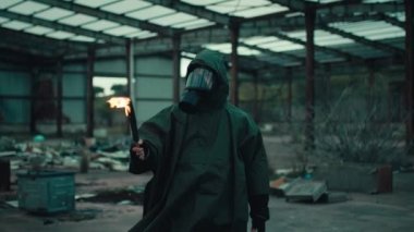 Gaz maskeli bir asker, meşaleyle yıkılan bir binada.