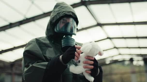 Un hombre con una máscara de gas encuentra un animal de peluche en un hospital destrozado por la guerra — Vídeos de Stock
