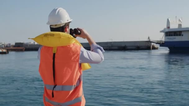 Jongen marine ingenieur controleert de aankomst van het schip uit de haven met een verrekijker — Stockvideo