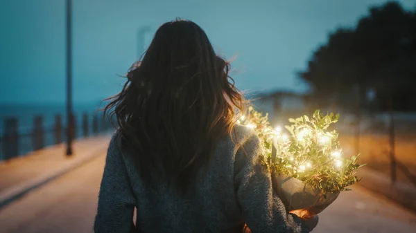 Gadis muda berjalan dengan karangan bunga tanaman dan lampu pesta di tangannya — Stok Foto
