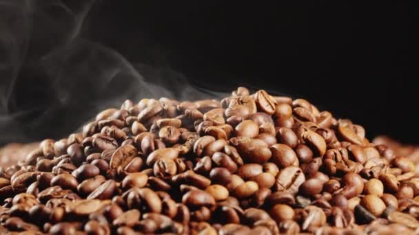 Arabica quality roasted coffee beans spin on a rotating plate with smoke — Stockvideo