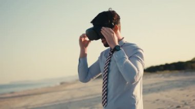 Young business guy boxing in virtual reality with headset at the beach
