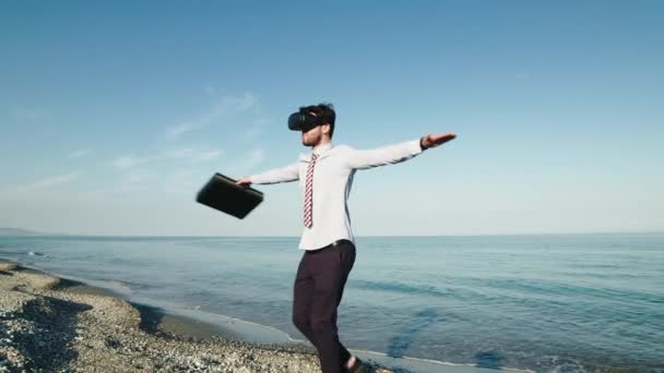 Happy Business guy spins on himself with virtual reality glasses on the beach — ストック動画
