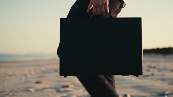 Businessman with black briefcase walks in the beach near the sea. — Stock Video