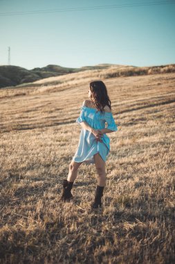 Güzel model kız doğada sarı bir tarlada poz veriyor. Dikey çekim.