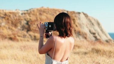 Beautiful girl makes shots with vintage camera in yellow countryside in summer.