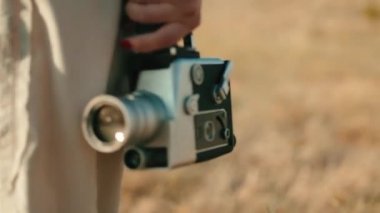 Vintage 8mm cinema camera in the hand of a girl walking in the countryside.