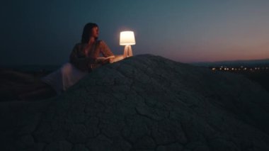 Beautiful girl enjoy the sunset on the mountain in the evening with abat jour lamp on the stones