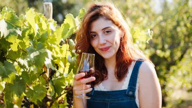 Young beautiful girl with goblet of red wine near the vineyards with quality grapes