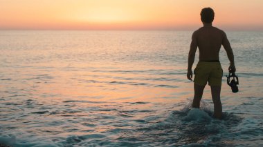 Sarı kostümlü adam şafakta sahilde eğlenir. El kamerasıyla çekim 