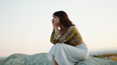 Disappointed young girl thinks about the future sitting on a rock in the countryside.